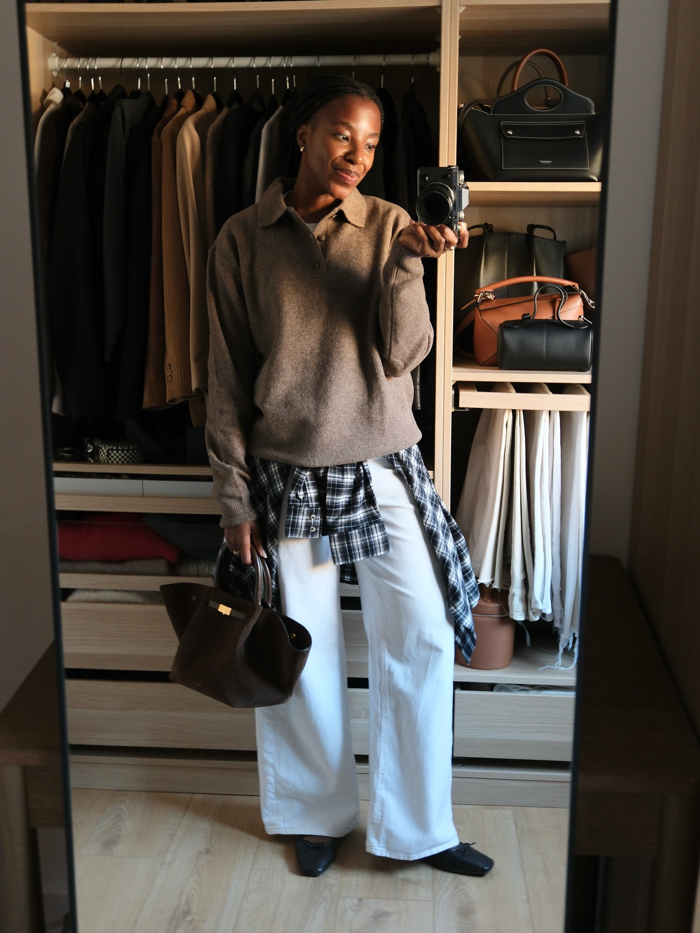 taffy msipa wears a brown jacket, check shirt and white jeans in front of her closet