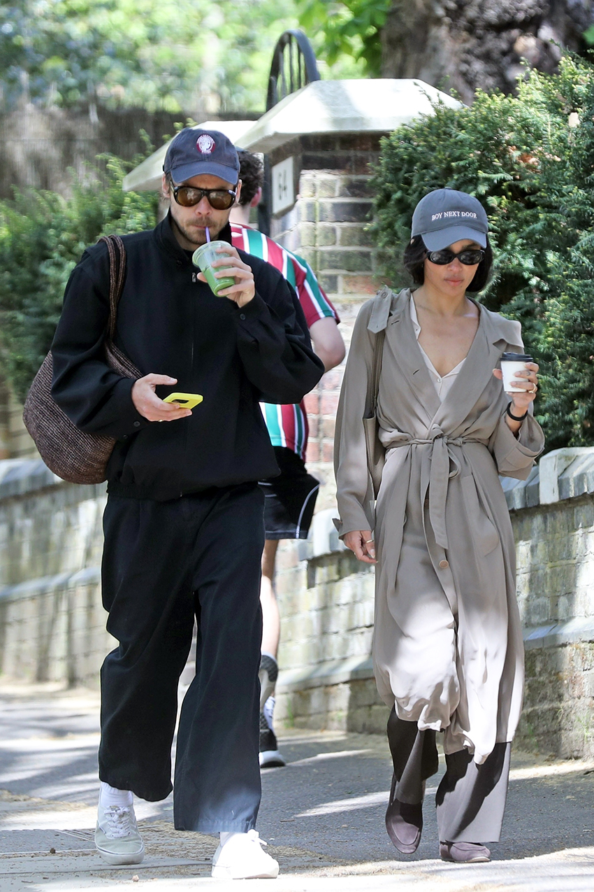 Zoe Kravitz wearing a navy baseball cap, tan trench coat, white blouse, black pants, and The Row soft loafers