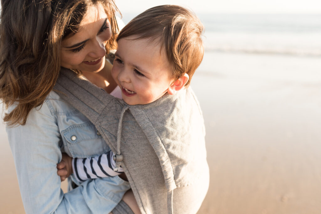 Babytrage-Test: Mutter mit lächelndem Kind in Trage am Strand.