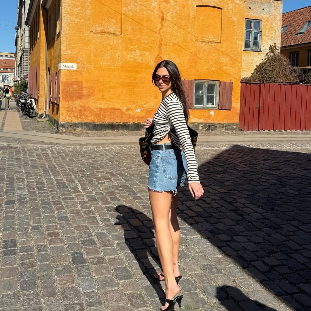 Dua Lipa in a striped tee, denim cutoffs and black accessories.
