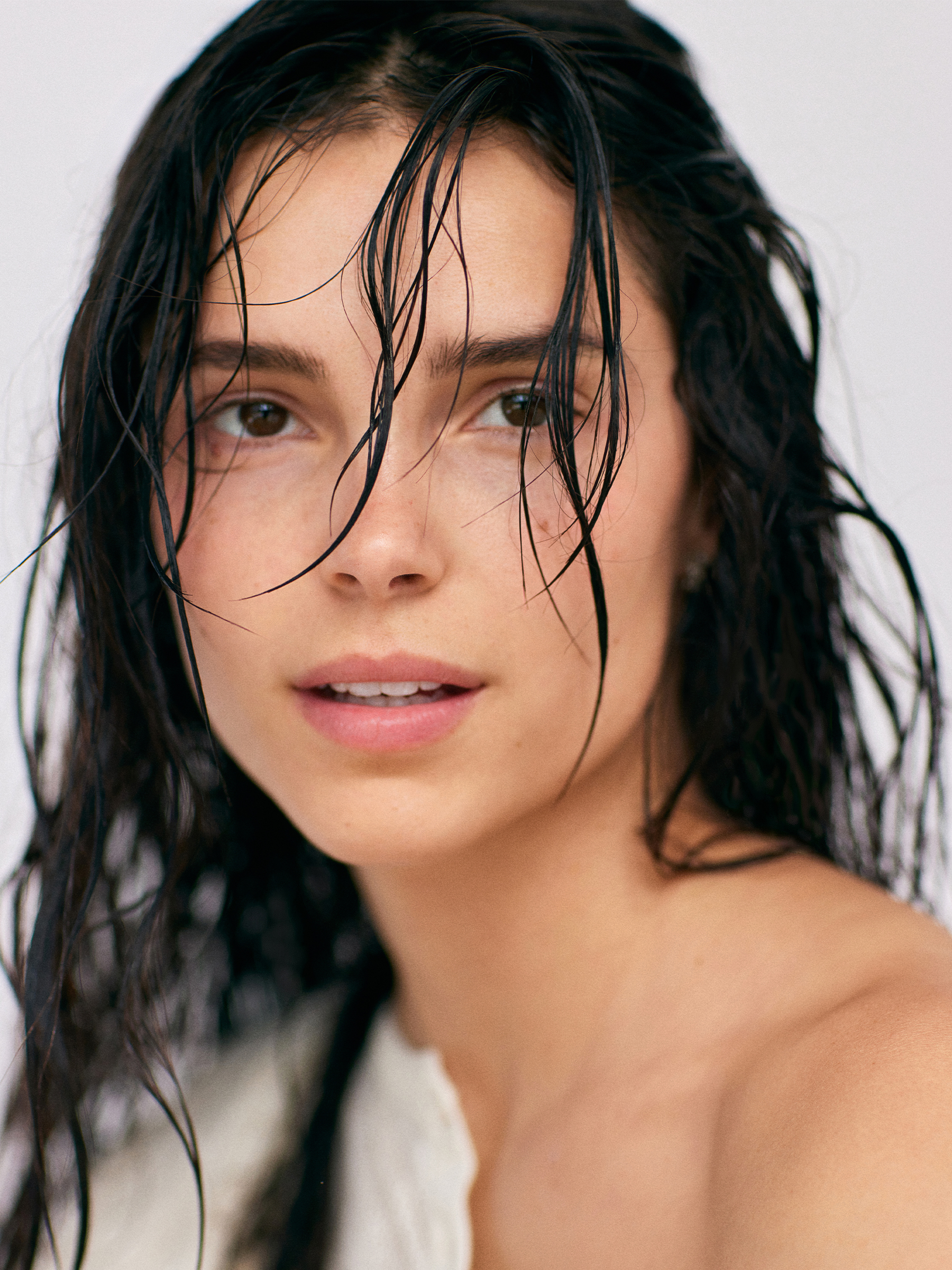 Actress Inde Navarette photographed by Emily Sandifer wearing an off-the-shoulder sheer cream dress. Her hair is wet with pieces falling in front of her face.