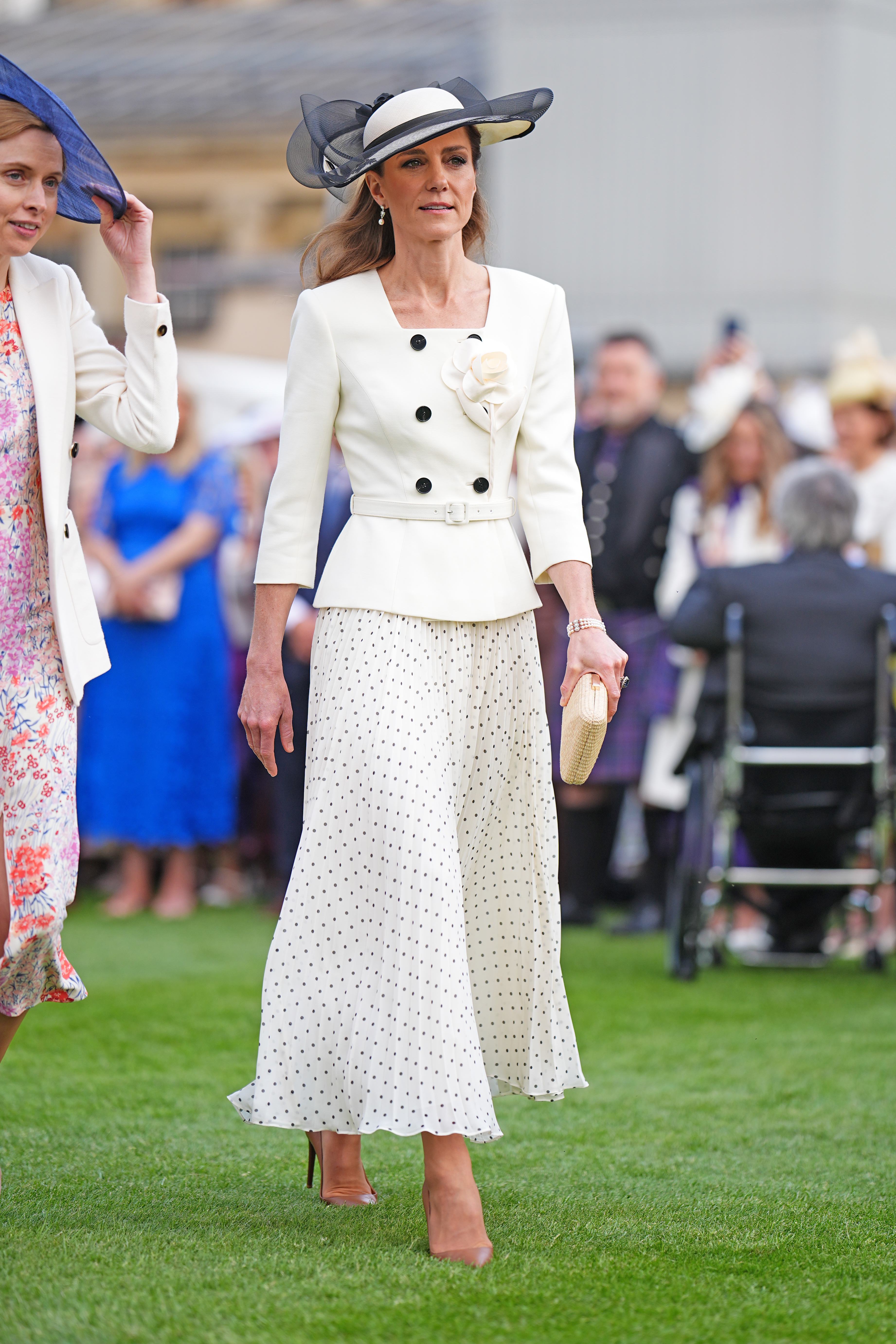 Kate Middleton wears a pleated polka-dot skirt with a white peplum jacket and beige heels.