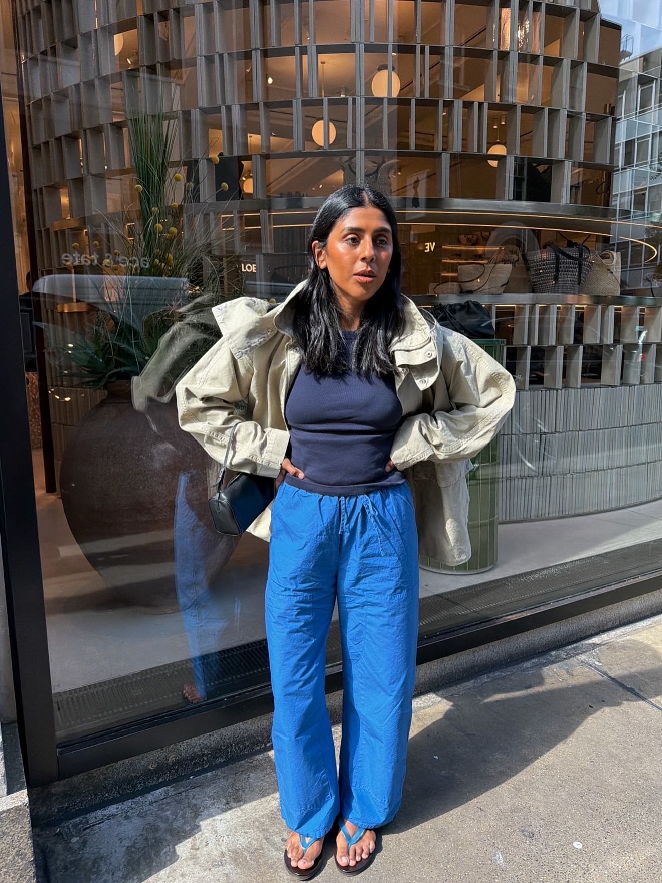 Influencer @monikh wears cobalt blue trousers with blue flip flops, a navy top and beige jacket.