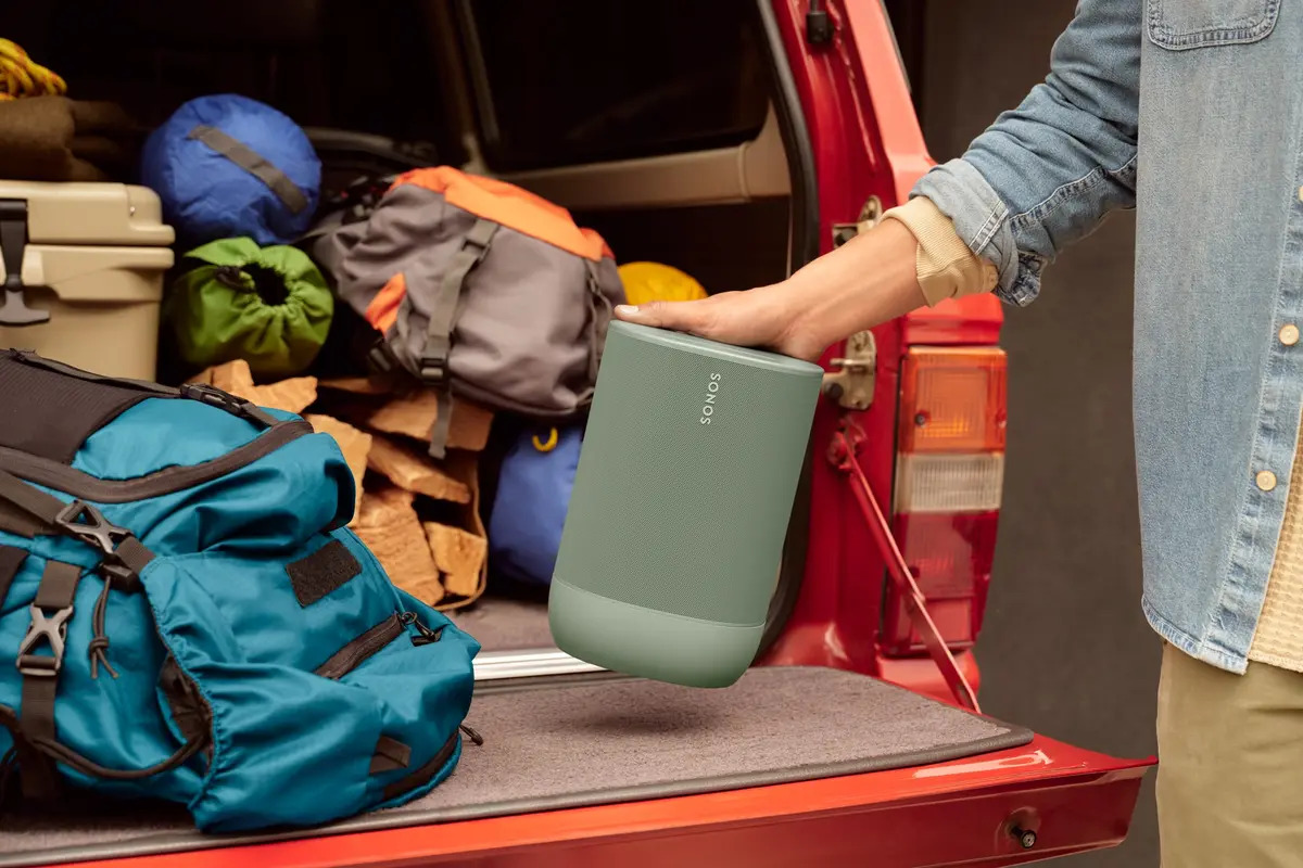 The Sonos Move 2 surrounded by items in the trunk of a car with a person’s hand lying on top.