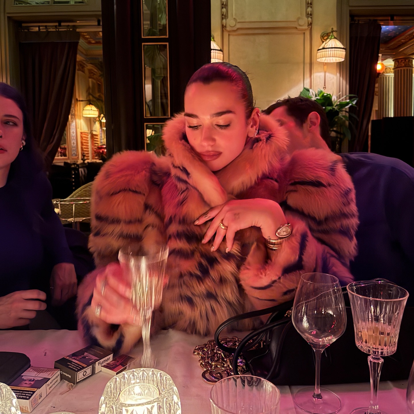 Dua Lipa sitting at dinner in a fur jacket.