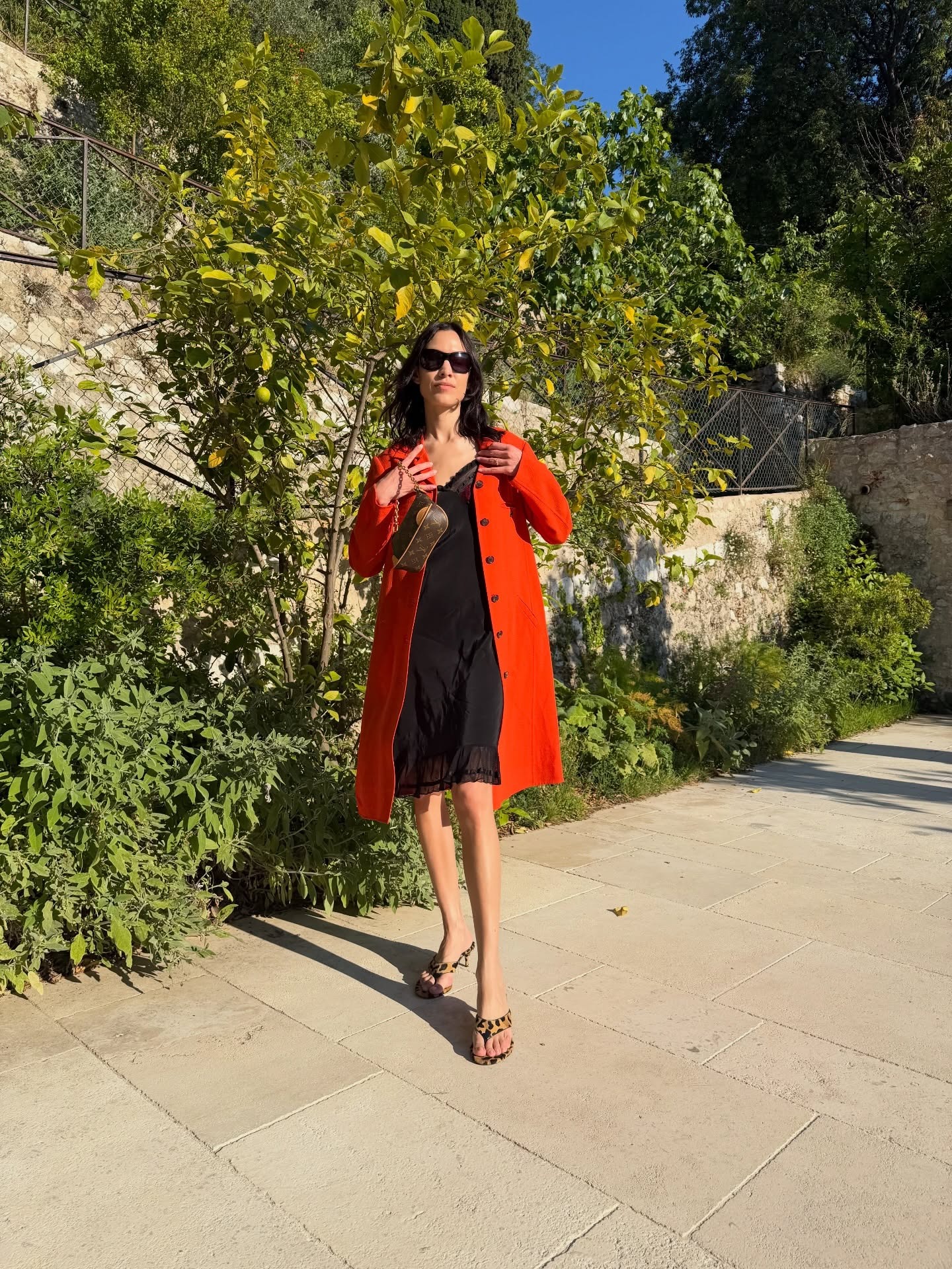 Alexa Chung wearing a red trench with a black slip dress, Louis Vuitton bag, and leopard-print Alaia thong high-heel sandals in France.