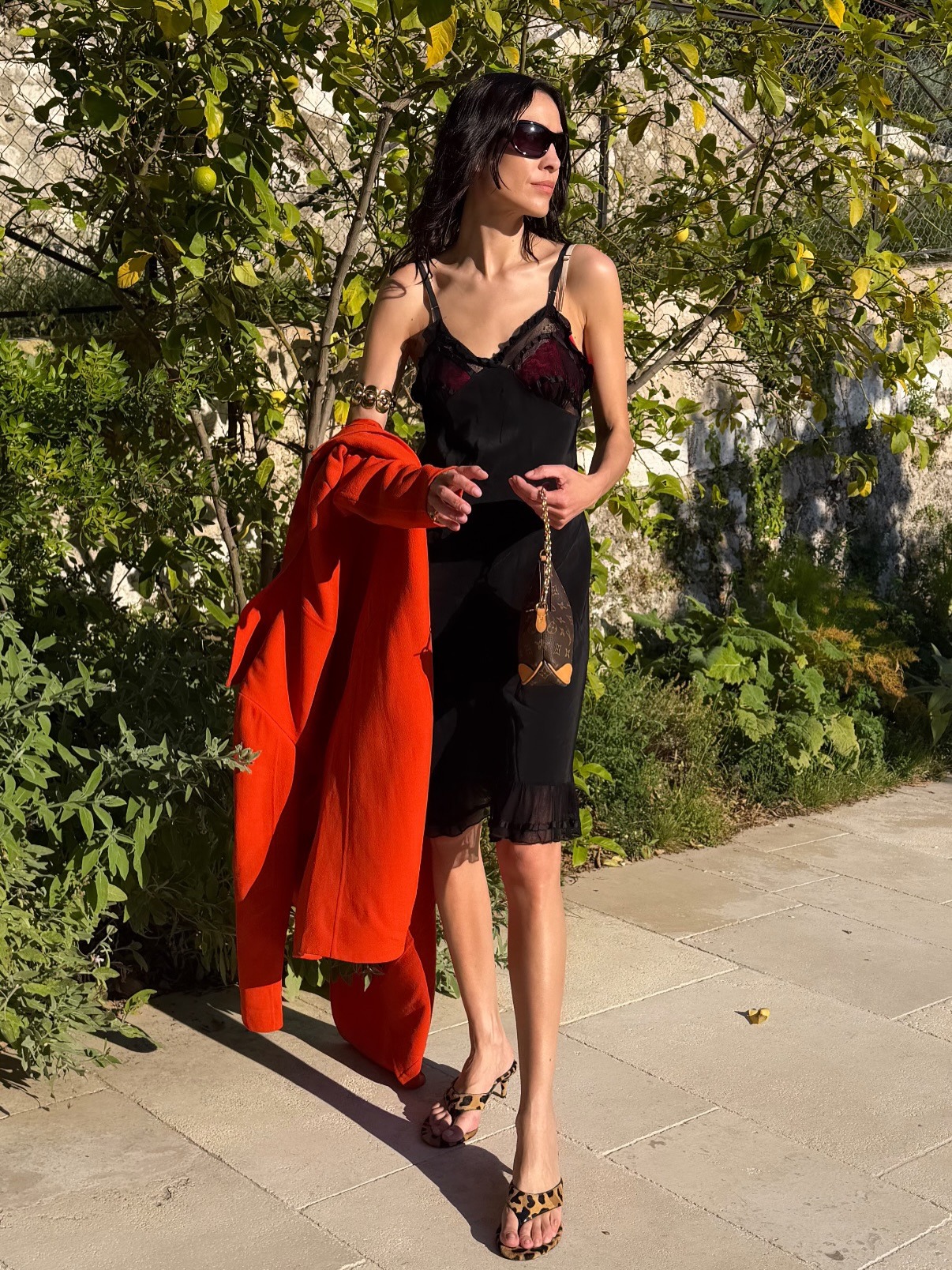 Alexa Chung wearing a red trench with a black slip dress, Louis Vuitton bag, and leopard-print Alaia thong high-heel sandals in France.