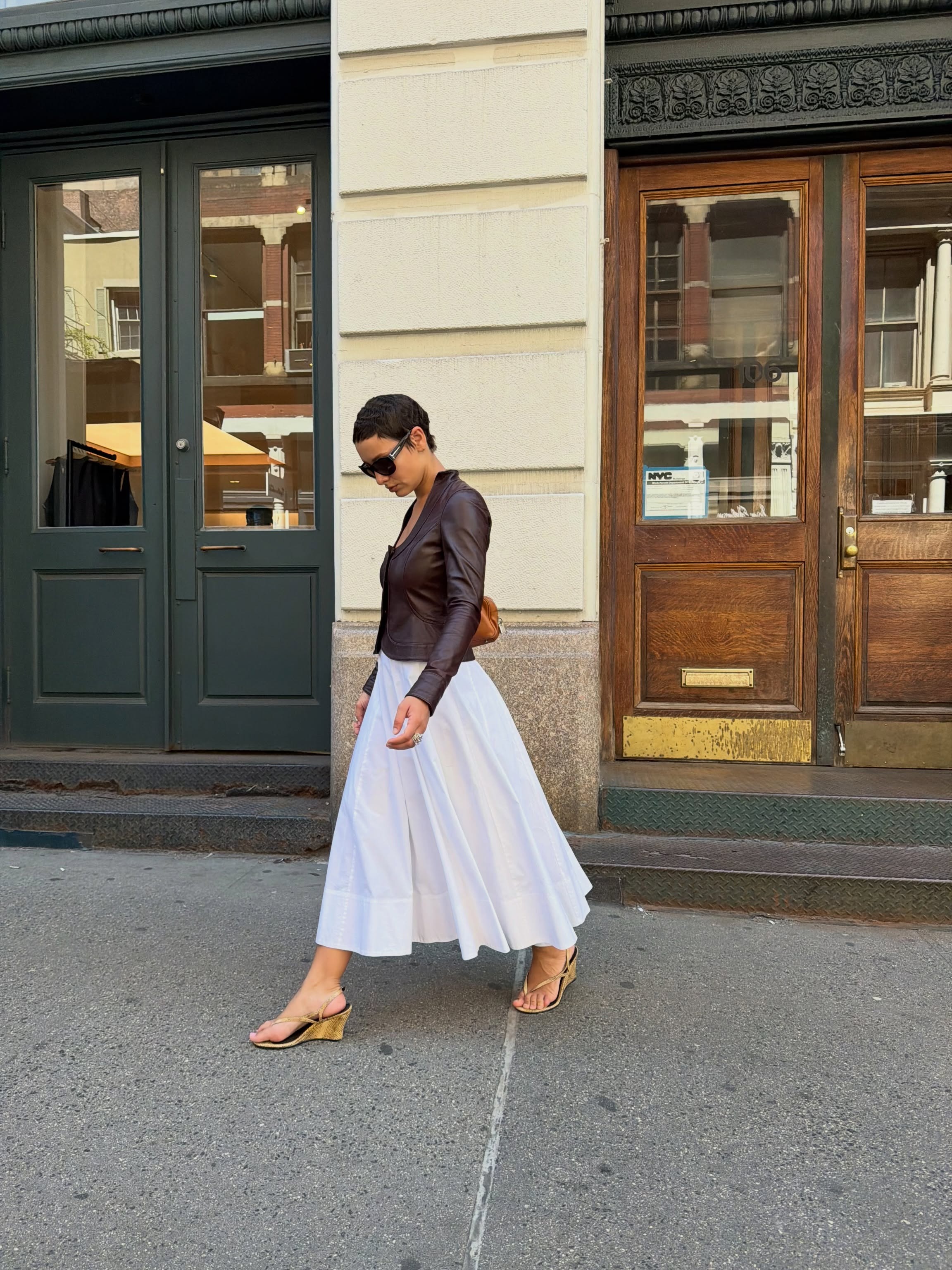 Aisha wears white dress, leather jacket, and wedged heels.