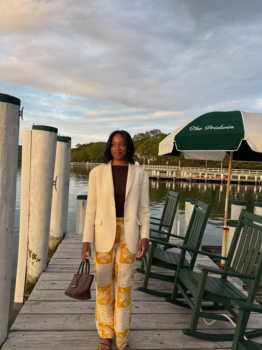 NYC woman wears a white blazder, brown top and butter yellow and white patchwork pants with a woven brown bag.