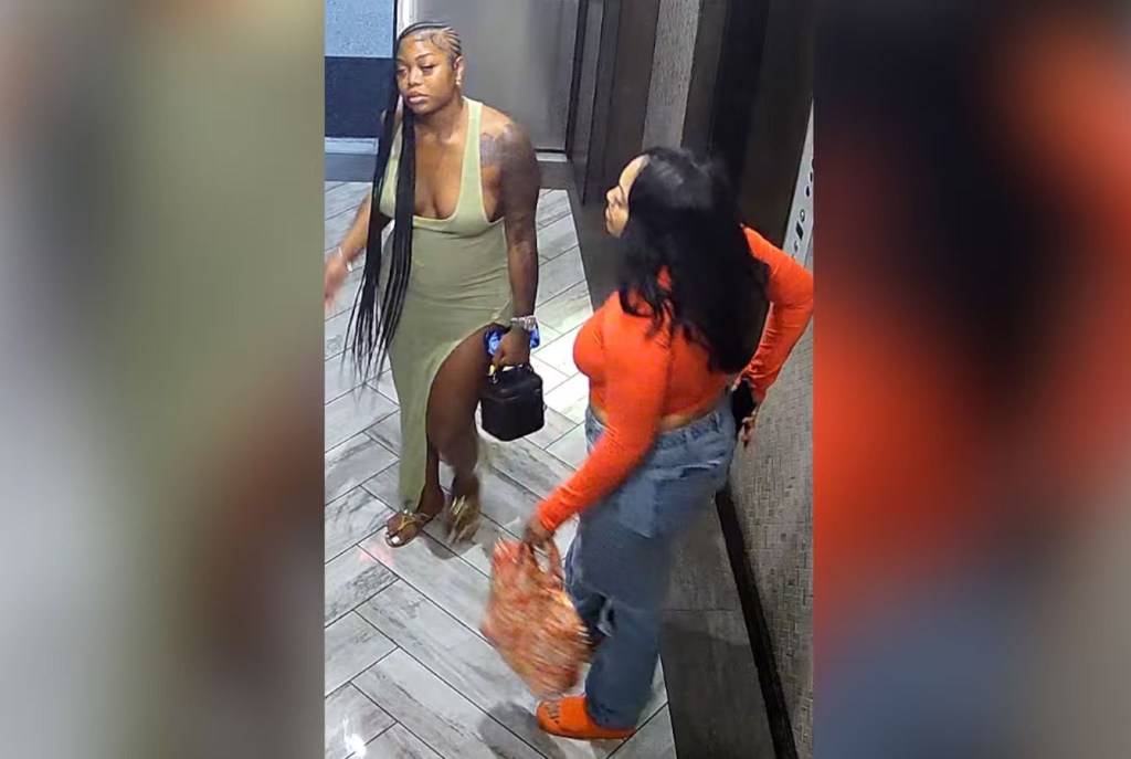 Two people, one wearing an orange outfit and the other wearing a green outfit, standing in a hallway.