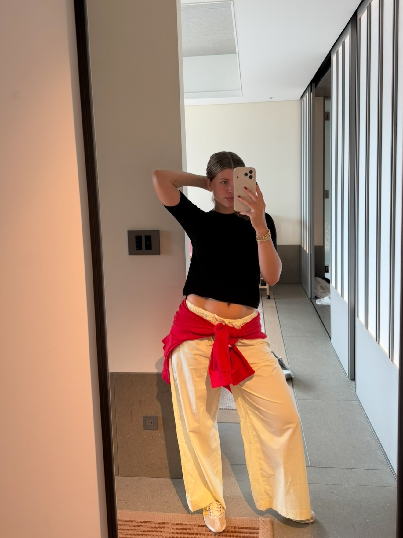 Sofia Richie Grainge wears a black tee, white drawstring pants, white sneakers, and a red sweater.
