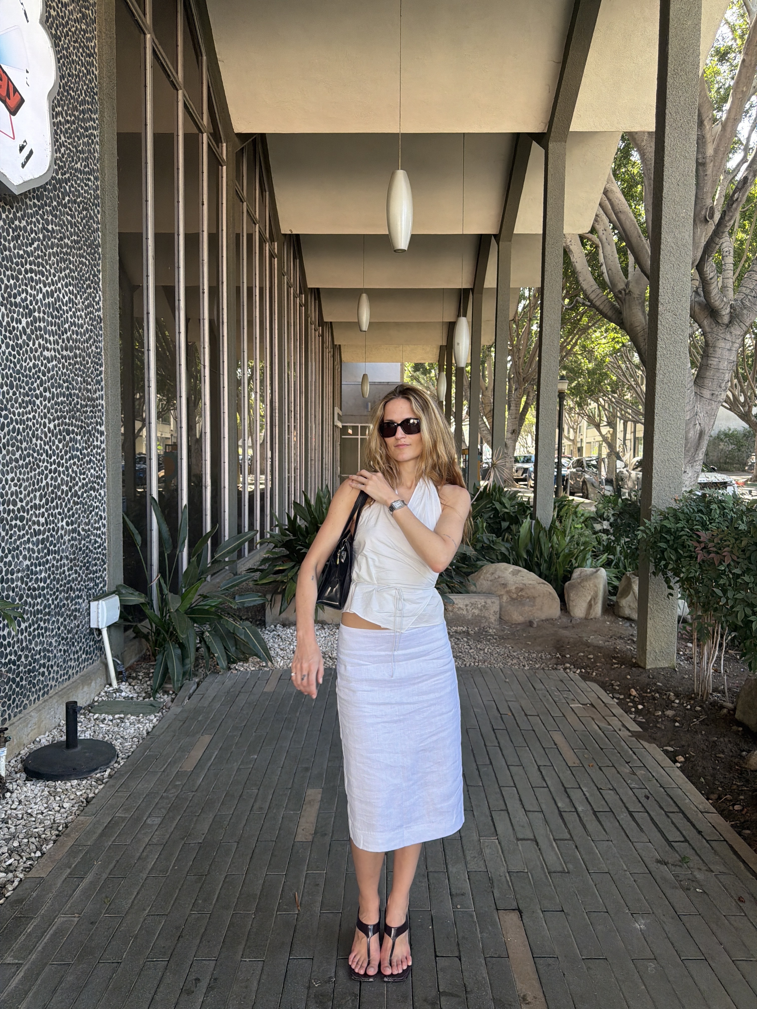 @elizagracehuber wearing a white St. Agni top, white Reformation knee-length skirt, and stretch-thong sandals.