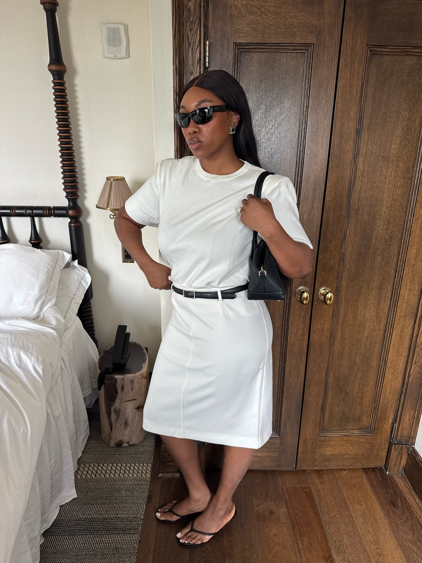 @nnenaechem wearing a white T-shirt, white knee-length skirt, and black strappy sandals.
