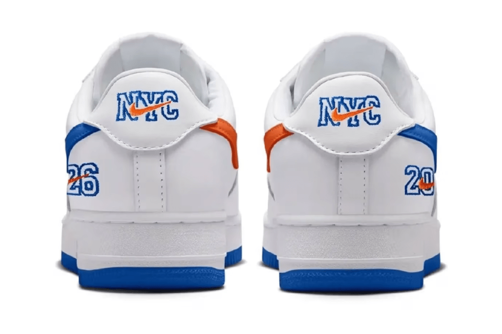 A pair of white sneakers with blue and orange accents, featuring the "NYC" logo and the number "26" printed on the sides.