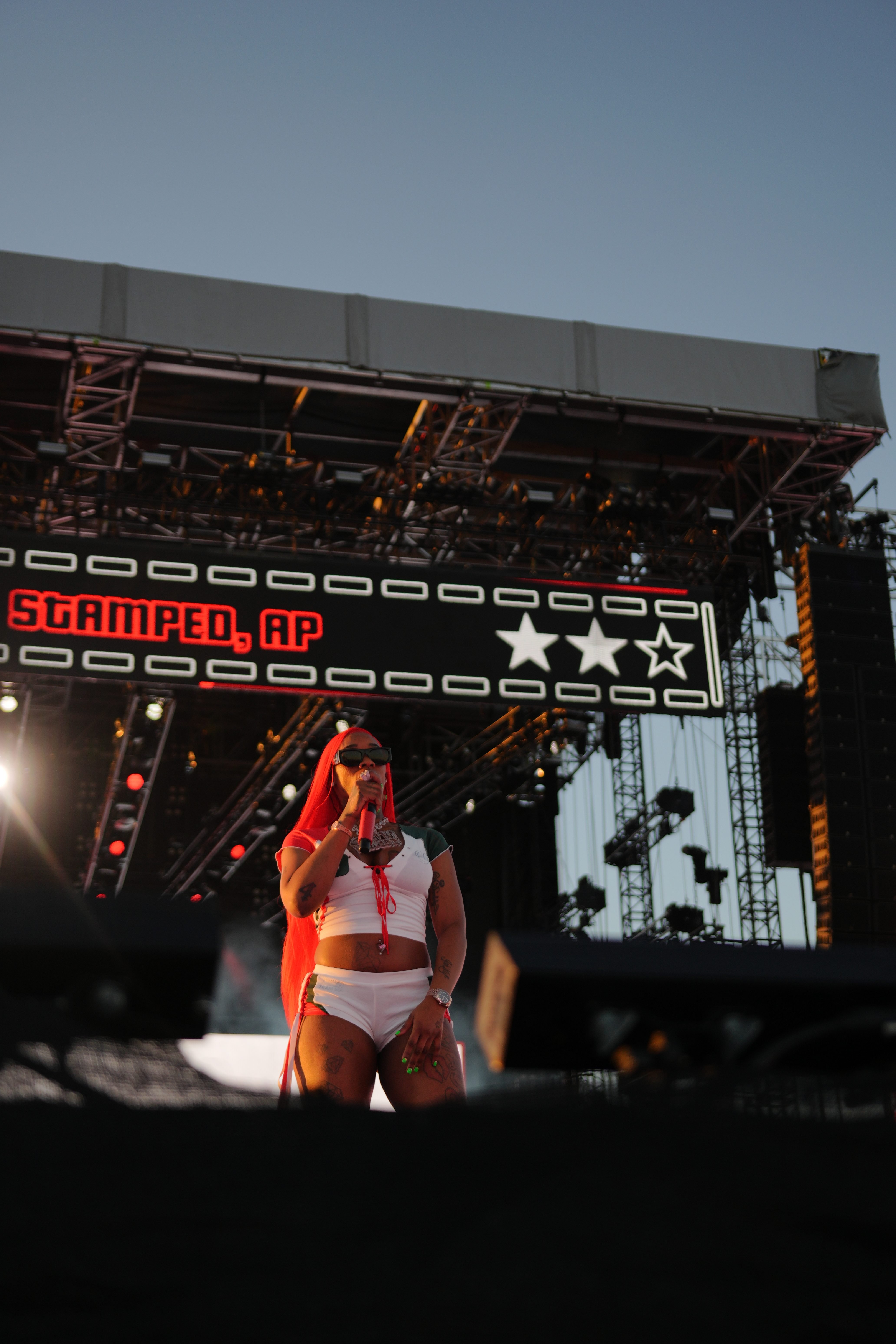 A performer wearing a red outfit stands on a stage with the text "Stamped, AP" displayed above.