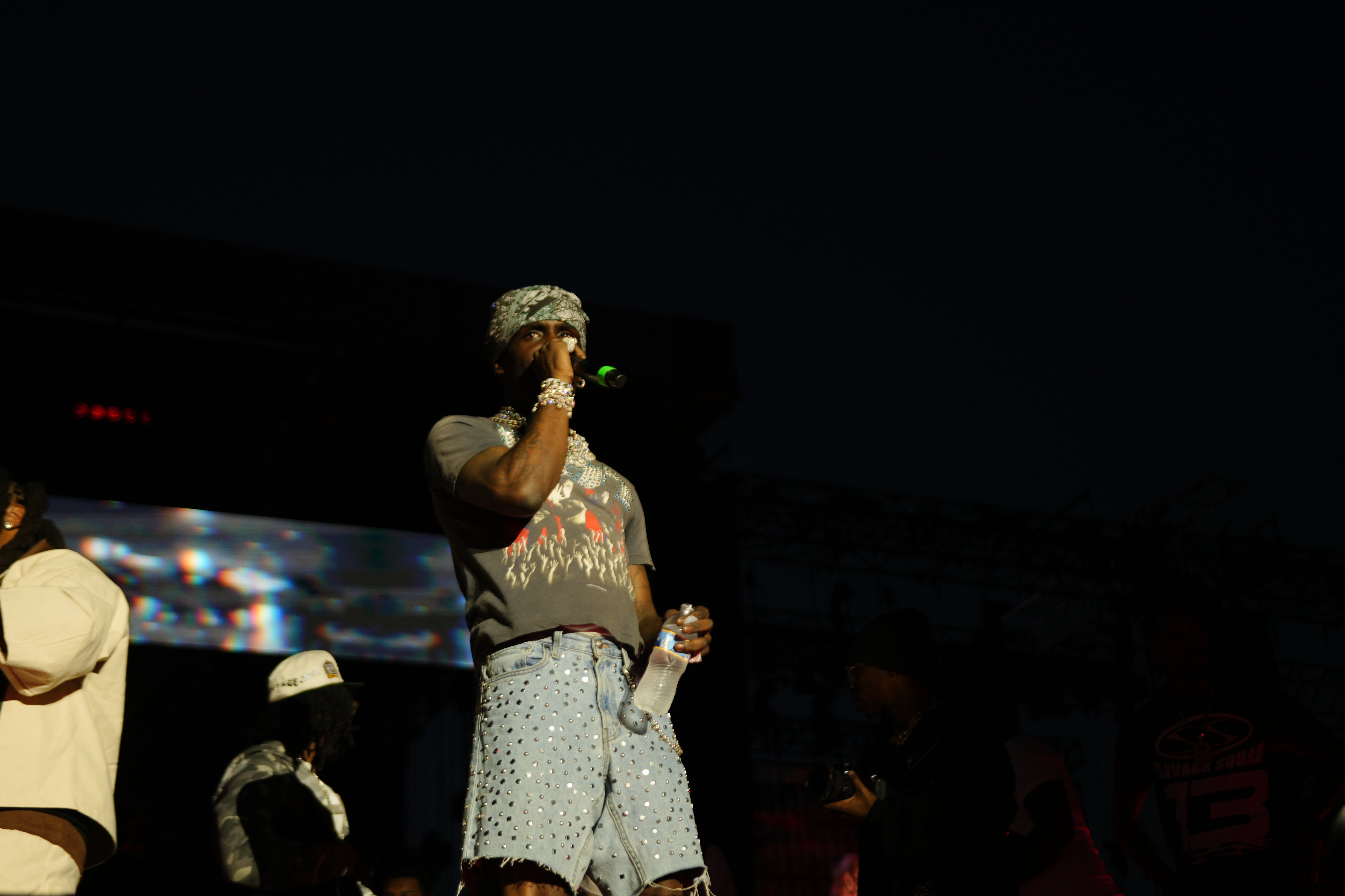 A performer on stage wearing a camouflage hat and patterned outfit, holding a microphone and singing into it.