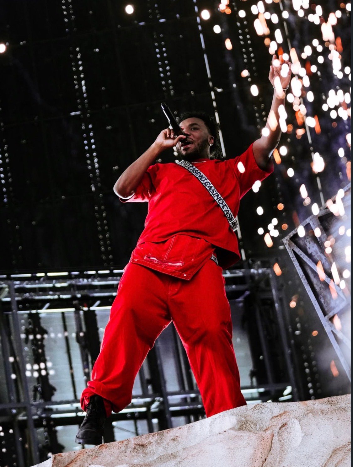 A person wearing a red outfit with text "DONDA SEASON" performing on stage with bright lights and sparks in the background.