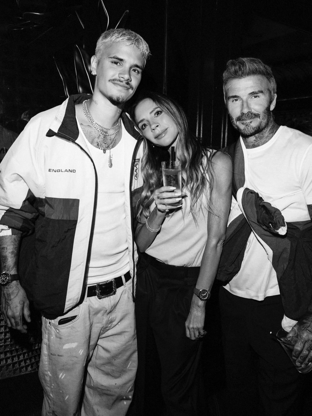 Victoria Beckham poses for a photo wearing a beige tank top with black tailored trousers.