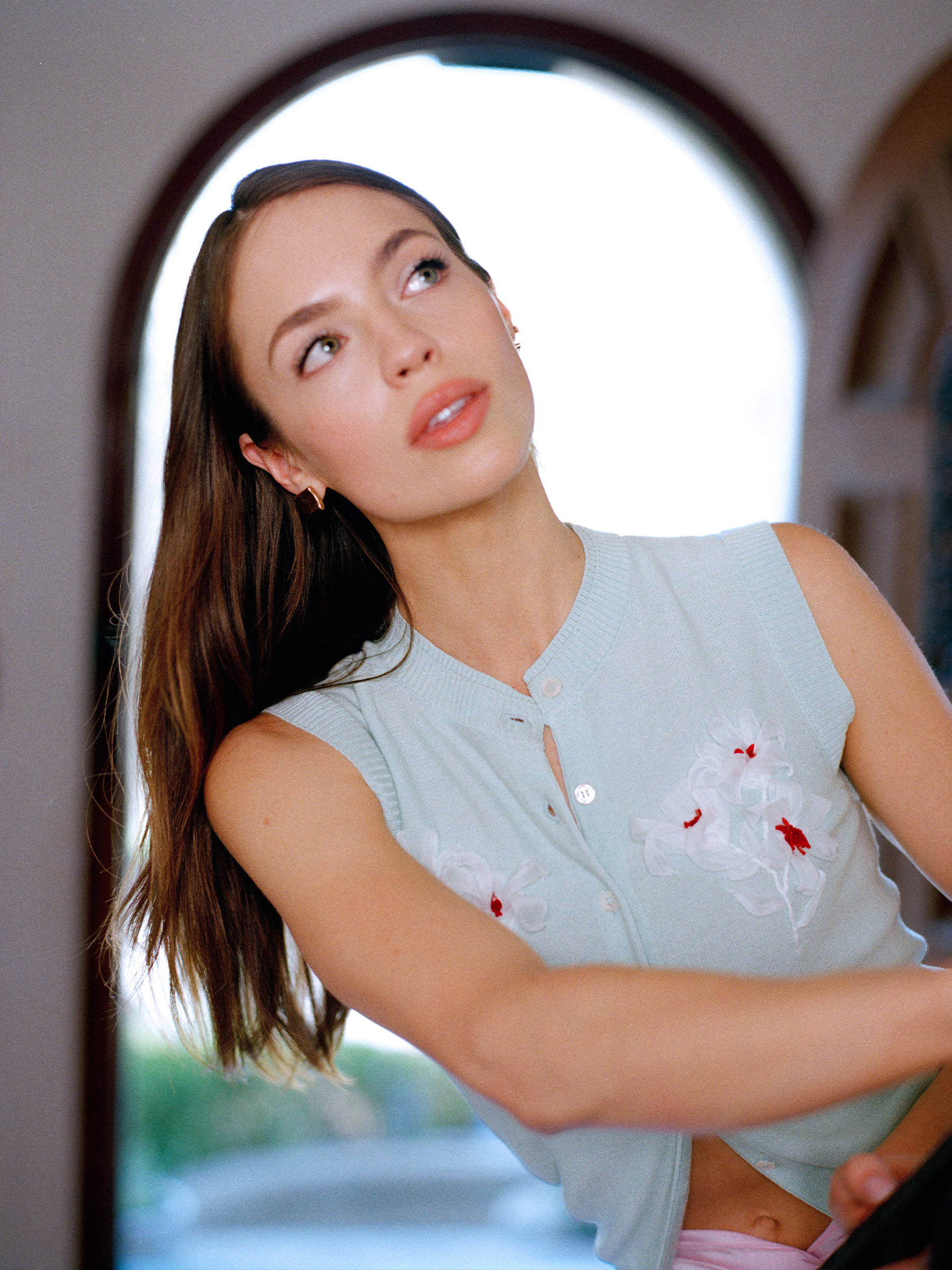 Claudia Sulewski wearing a pale blue button-front sweater vest with white and red floral embroidery.