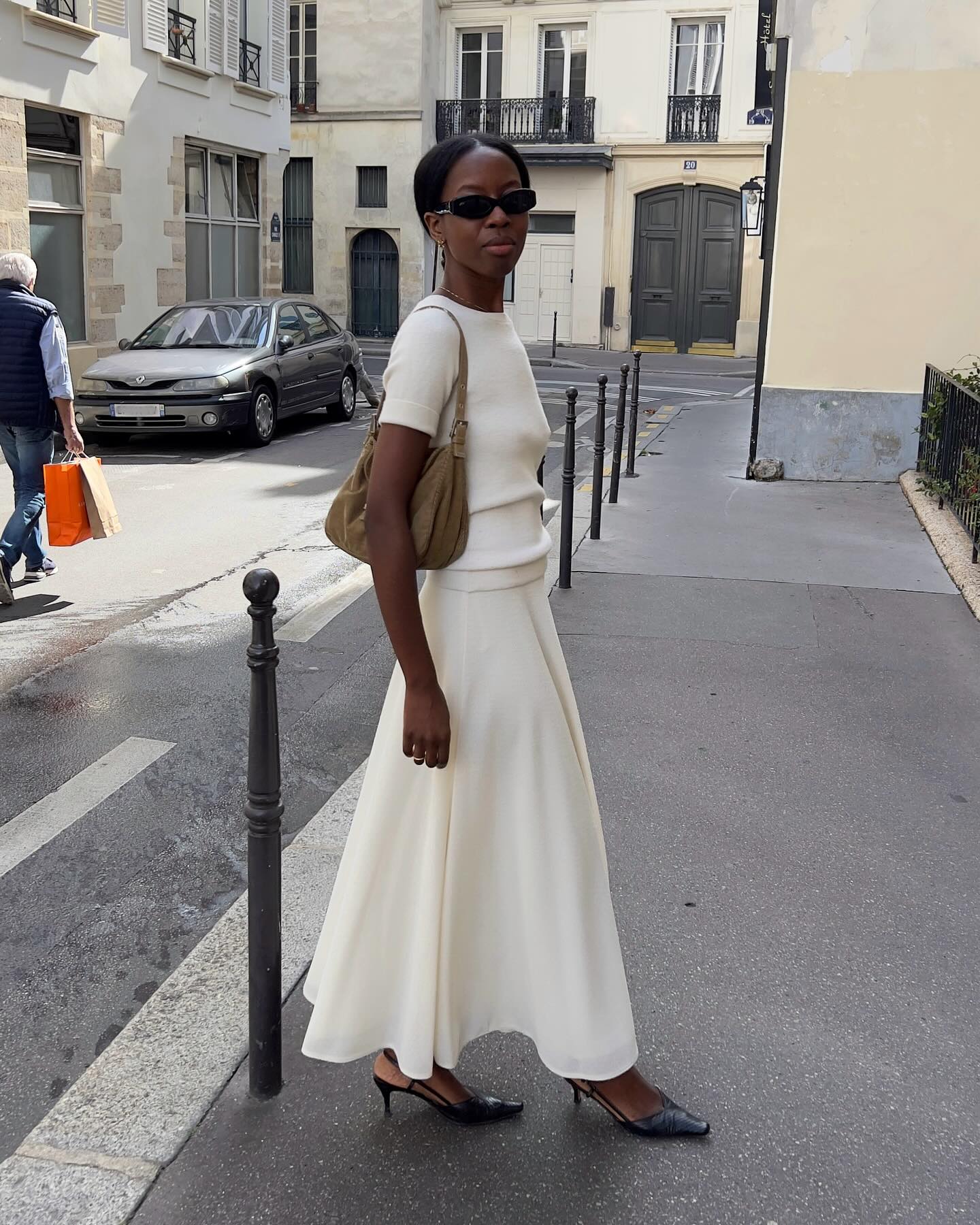 An image of an influencer in Paris wearing a white knit short-sleeve top, white skirt and black slingback heels