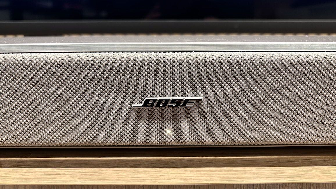 Nahaufnahme der Front der Bose Lifestyle Ultra Soundbar. Die helle Stoffbespannung, das Bose-Logo sowie die kleine Status-LED auf der Vorderseite sind zu erkennen.