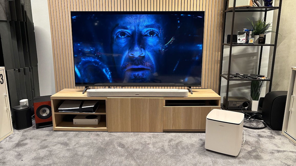Die Bose Lifestyle Ultra Soundbar steht unter einem Fernseher, daneben ist der kabellose Subwoofer aufgestellt. Auf dem Bildschirm läuft eine Filmszene.