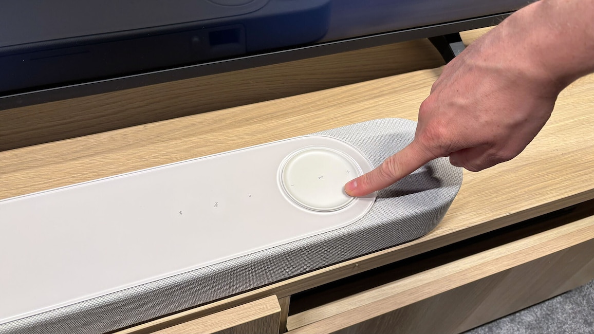 Eine Person bedient das große berührungsempfindliche Lautstärkerad auf der Oberseite der Bose Lifestyle Ultra Soundbar. Die Bedienelemente sind in die Glasoberfläche integriert.