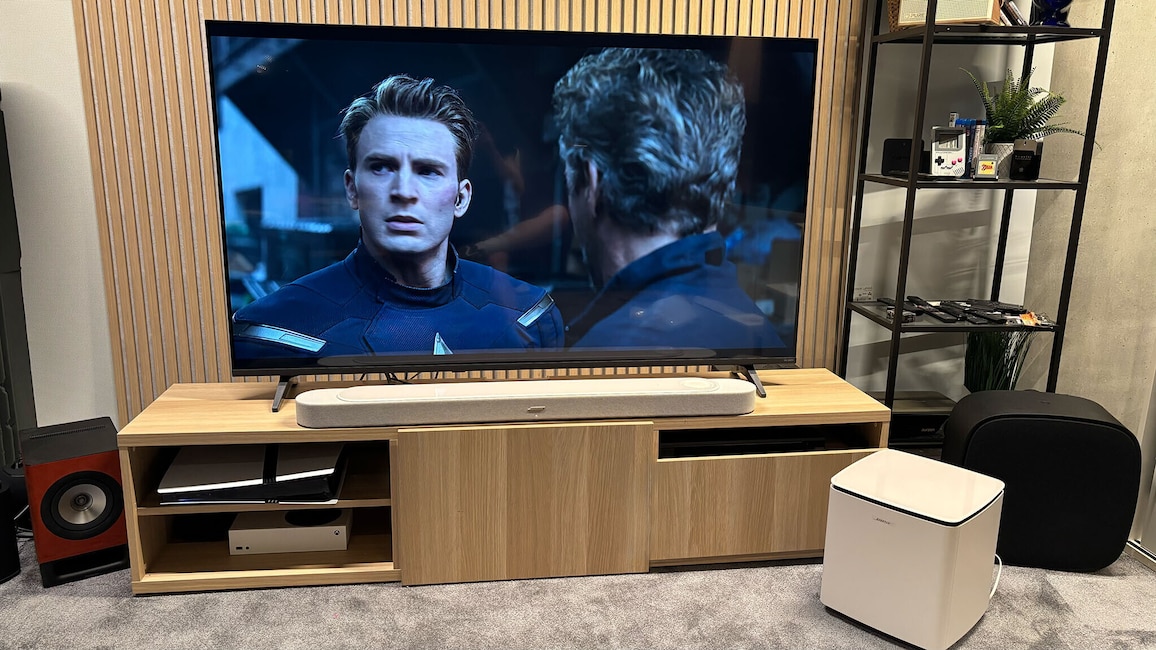 Die Bose Lifestyle Ultra Soundbar steht unter einem Fernseher, daneben der kabellose Subwoofer. Auf dem Bildschirm läuft eine Filmszene mit Captain America und Steve Rogers.