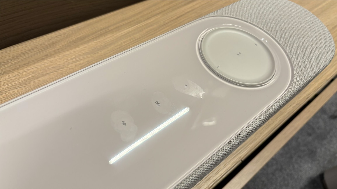 Nahaufnahme der Oberseite der Bose Lifestyle Ultra Soundbar. Zu sehen sind die Glasoberfläche mit Fingerabdruckspuren, die berührungsempfindlichen Bedienelemente sowie ein großes Lautstärkerad.