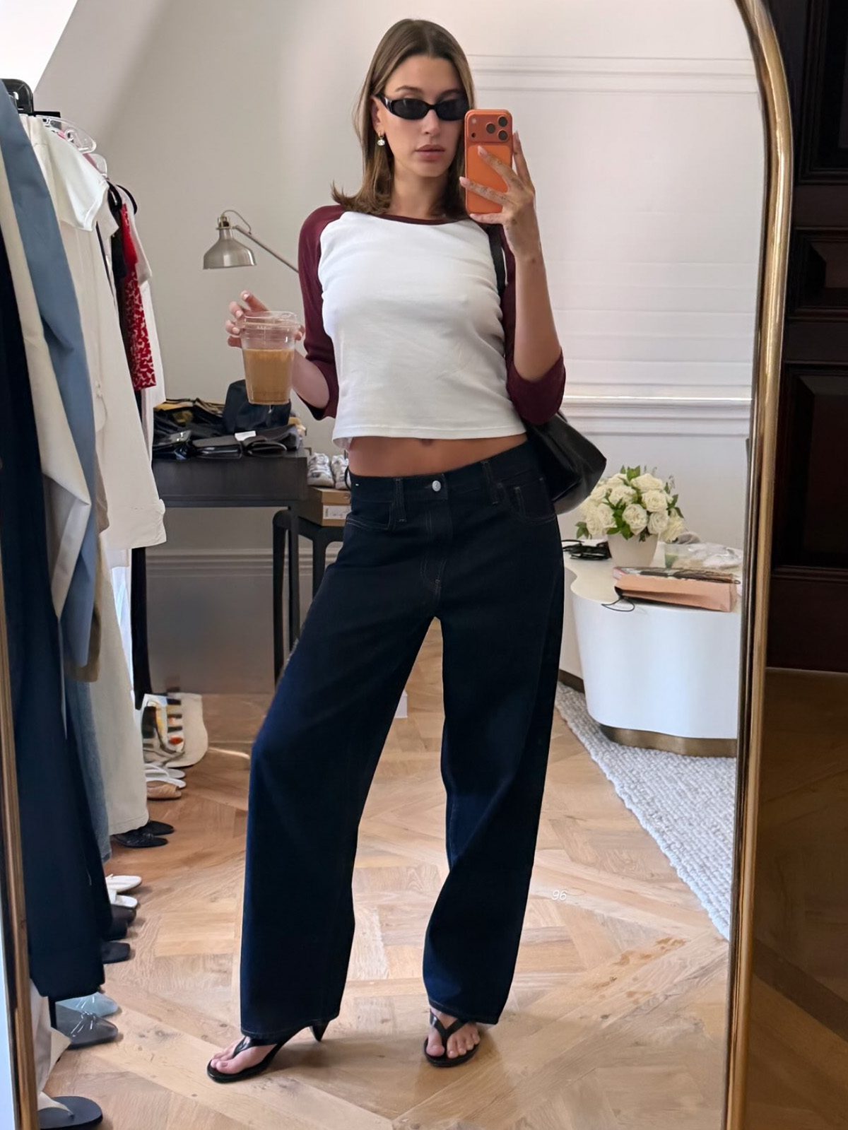 Hailey Bieber wearing a baseball tee with low-rise dark-wash jeans and cone-heel thong sandals.