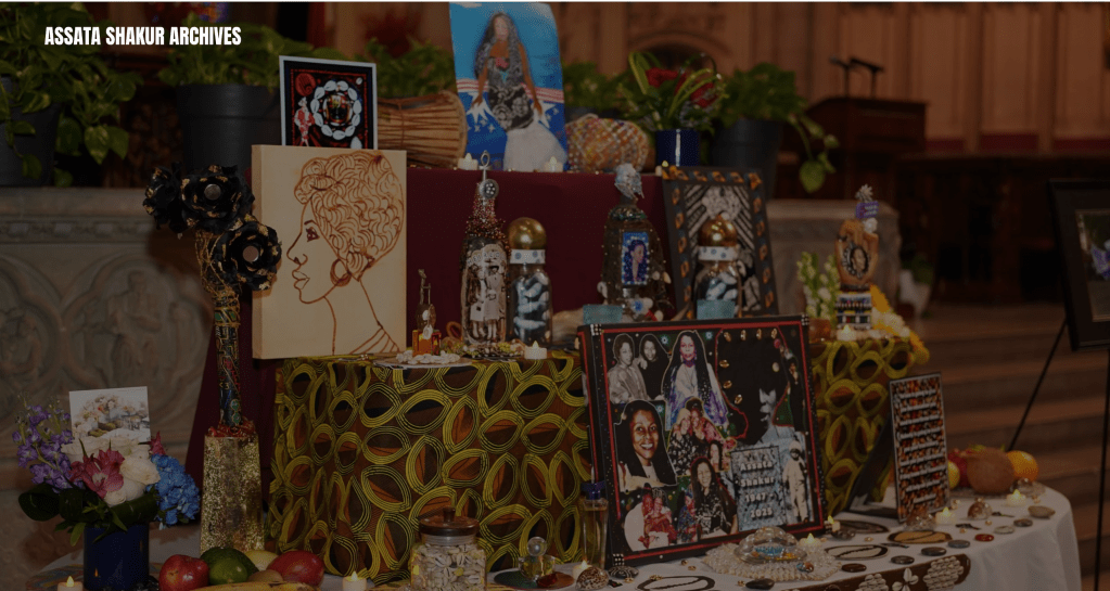 Assortment of framed artwork, photographs, and memorabilia displayed on a table, including images of a woman and various cultural symbols.