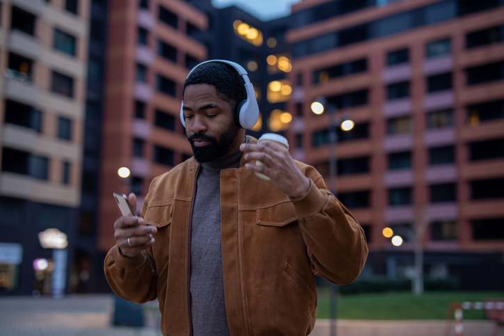 Young man enjoying music walking in city with coffee