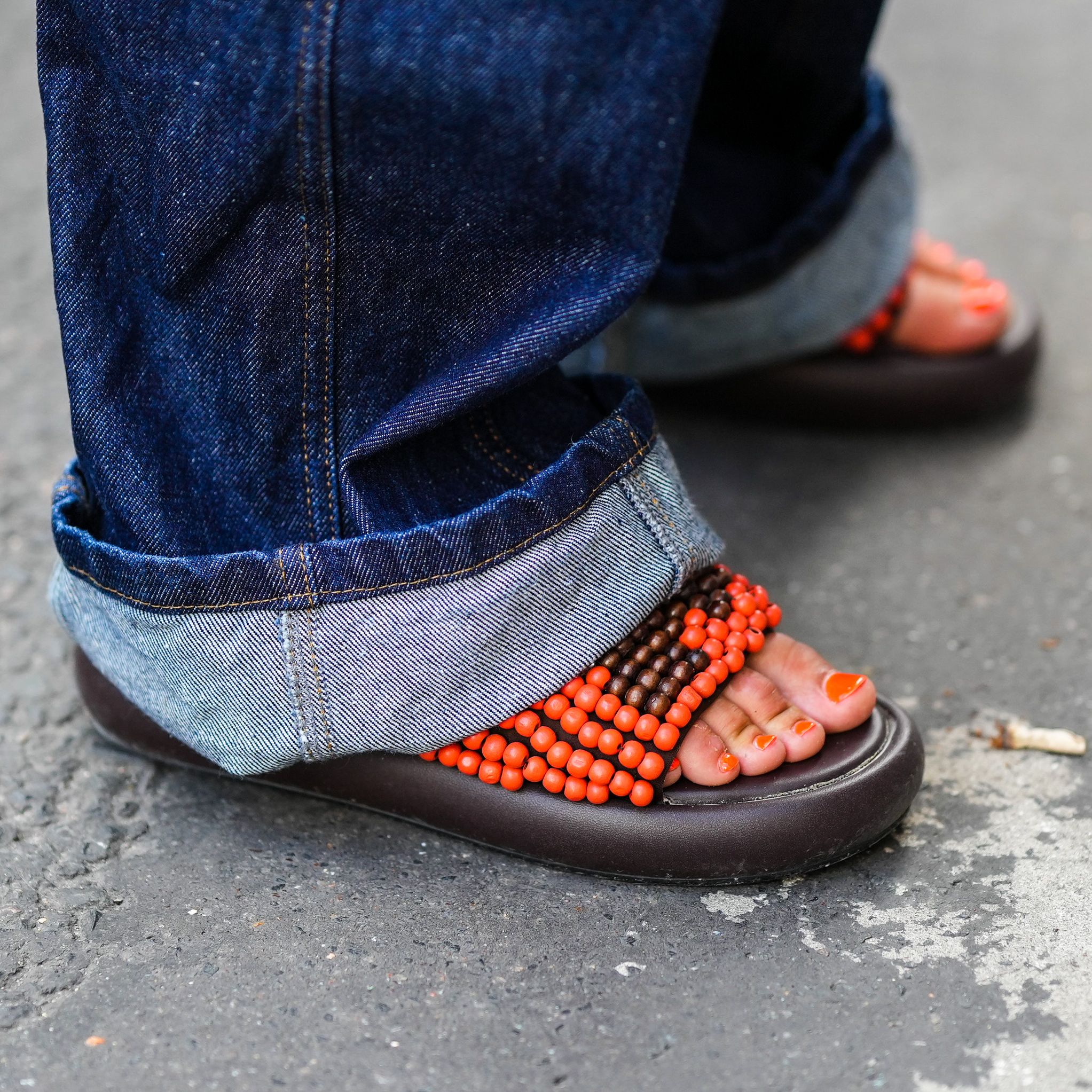 Feet in black sandals with an orange pedicure.