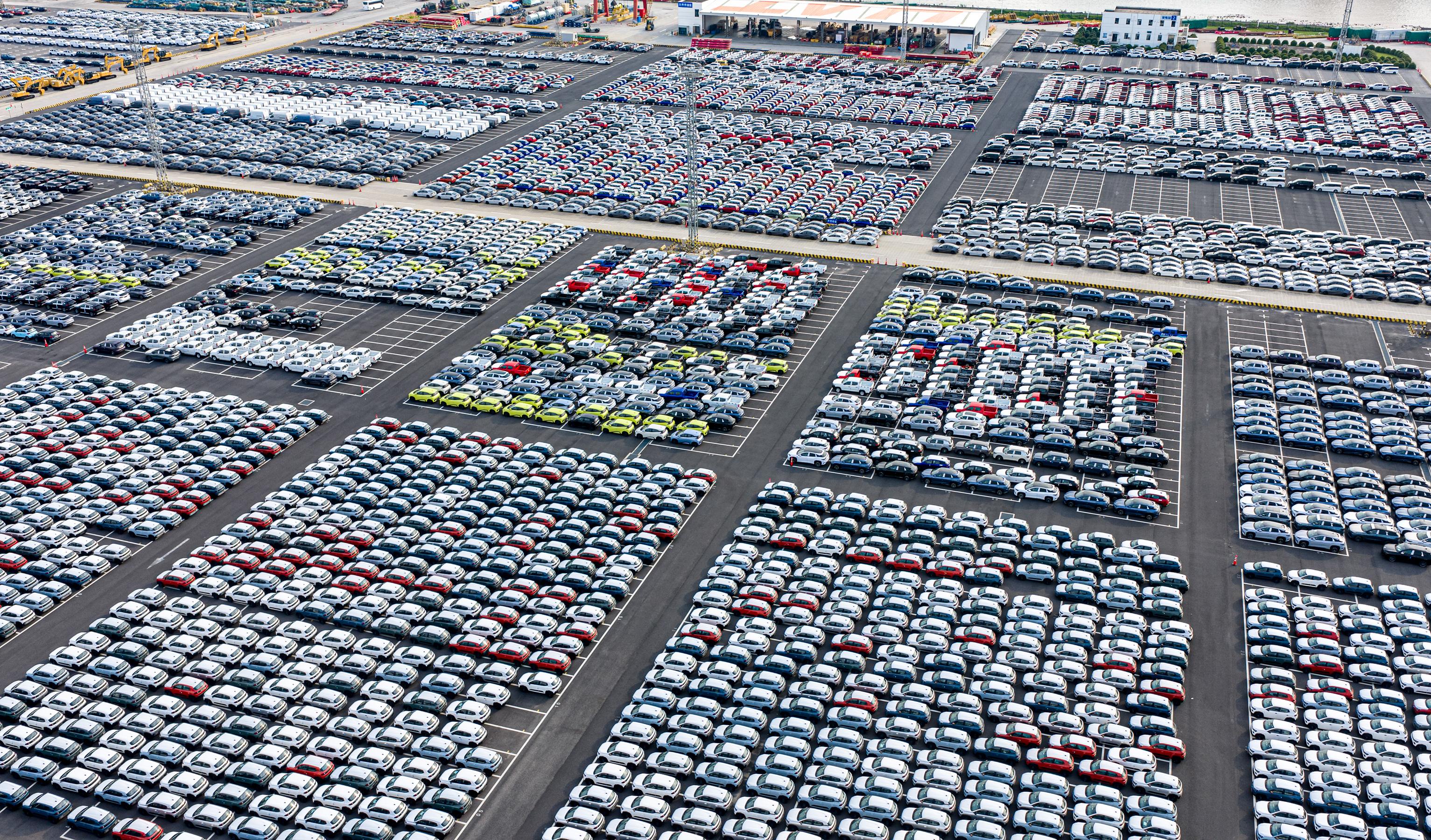 Hundreds of cars neatly arranged can be seen in an enormous parking lot from above. 