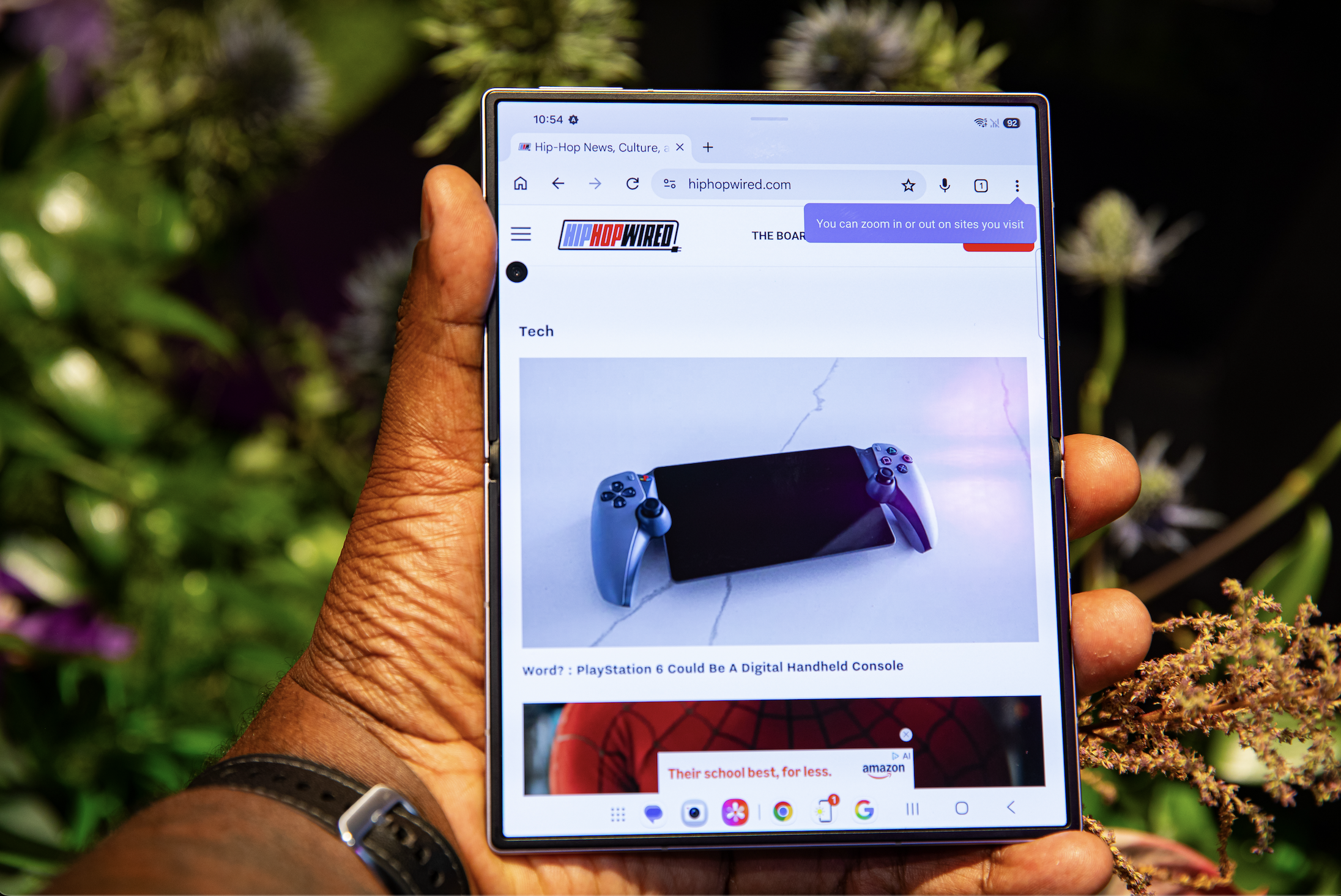 A hand holding a tablet displaying a PlayStation 6 controller on a website called HipHopWired.com