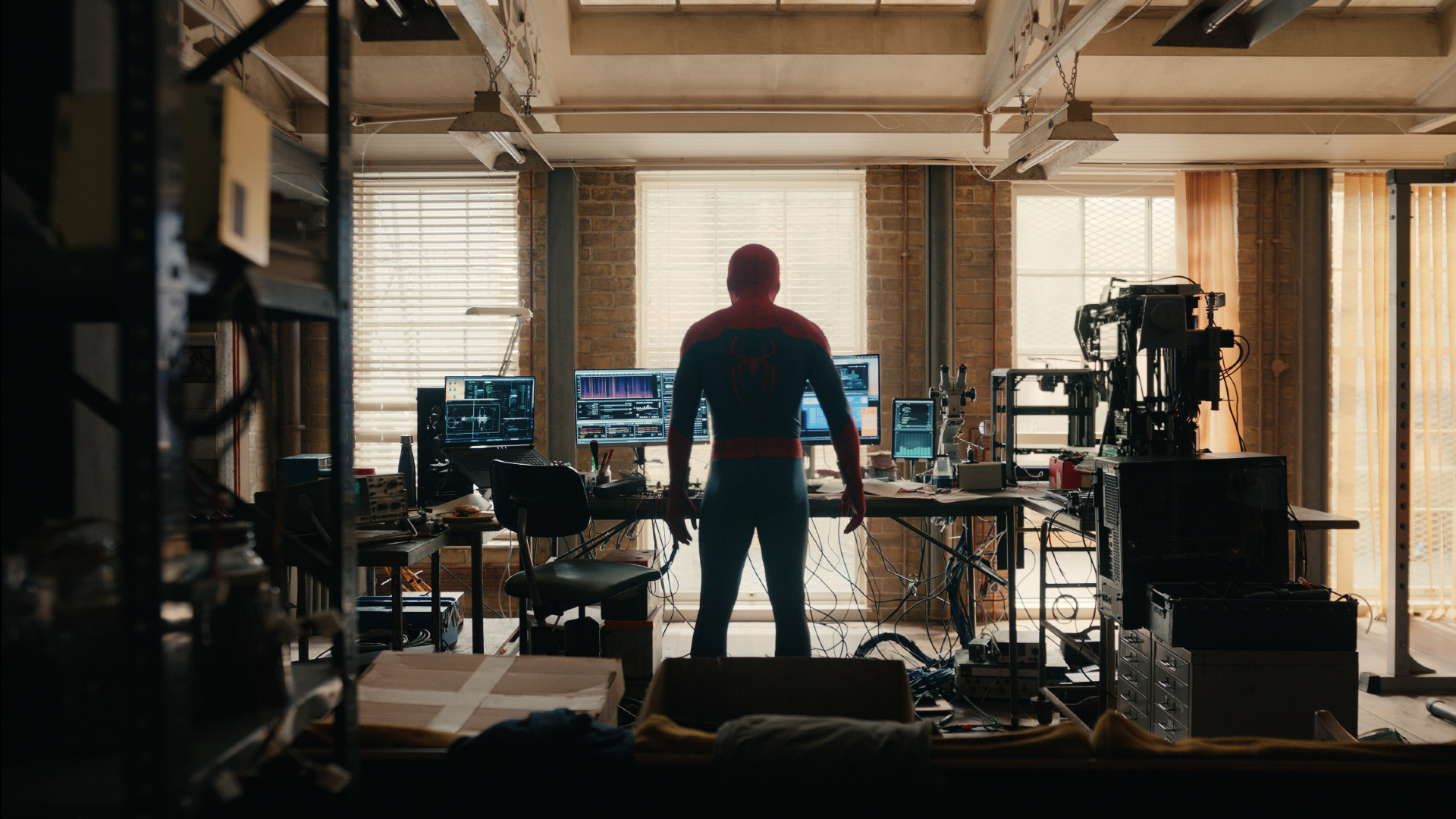 A person in a red and blue costume stands in a cluttered room filled with audio and video equipment.