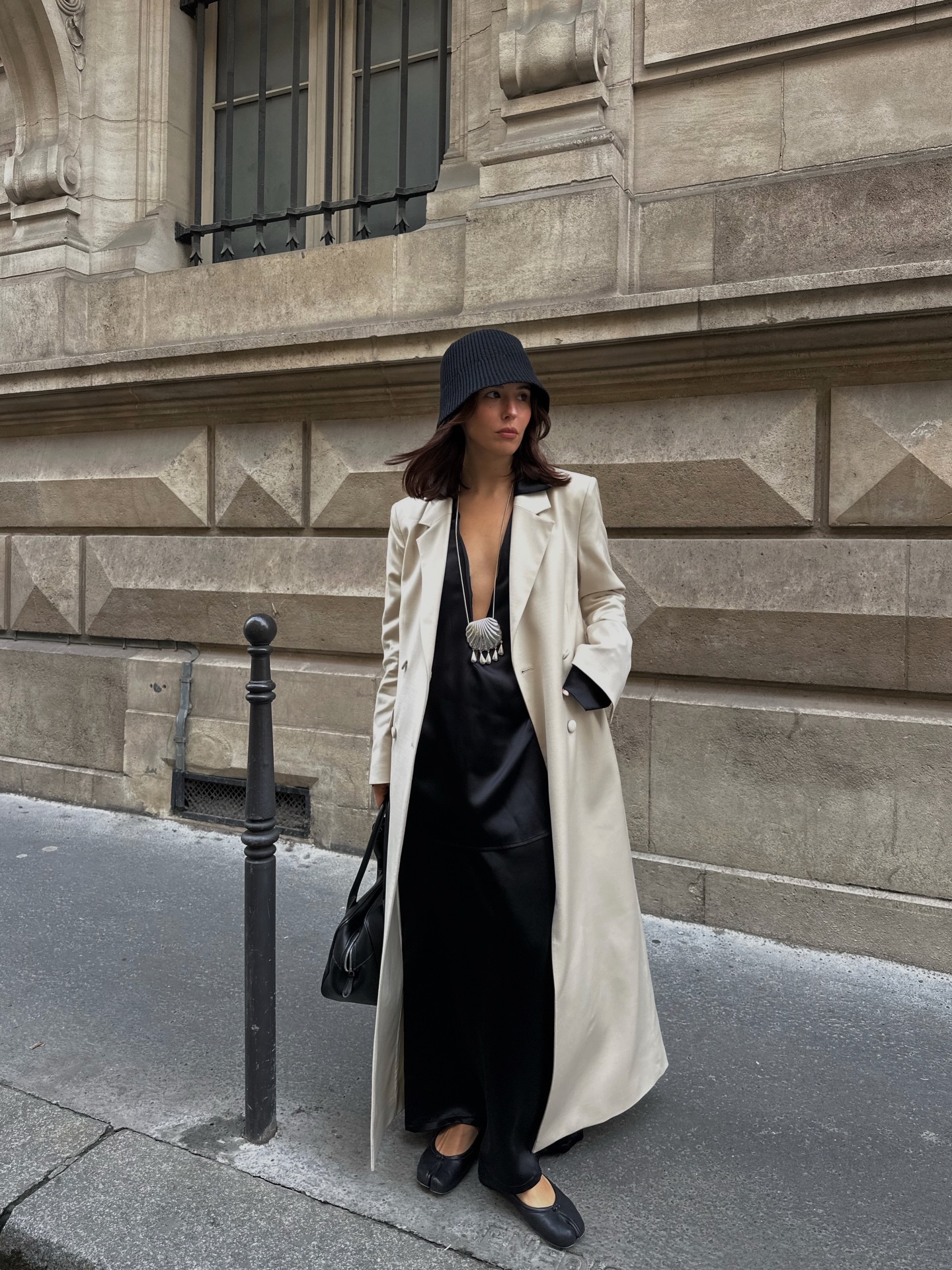 An image of @deborabrosa wearing satin trousers with a long opera coat and bucket hat.