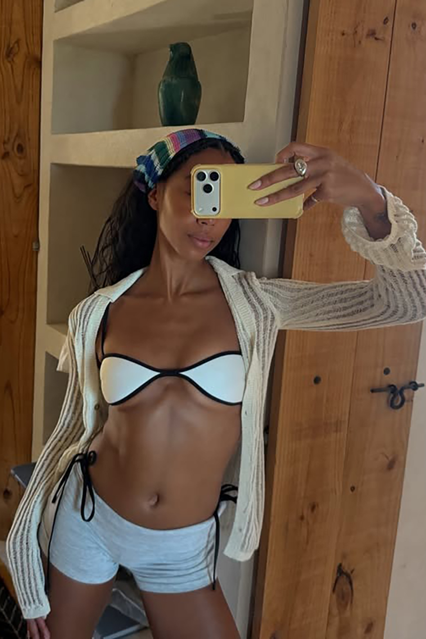 a woman wearing a head scarf, white bikini, and gray shorts