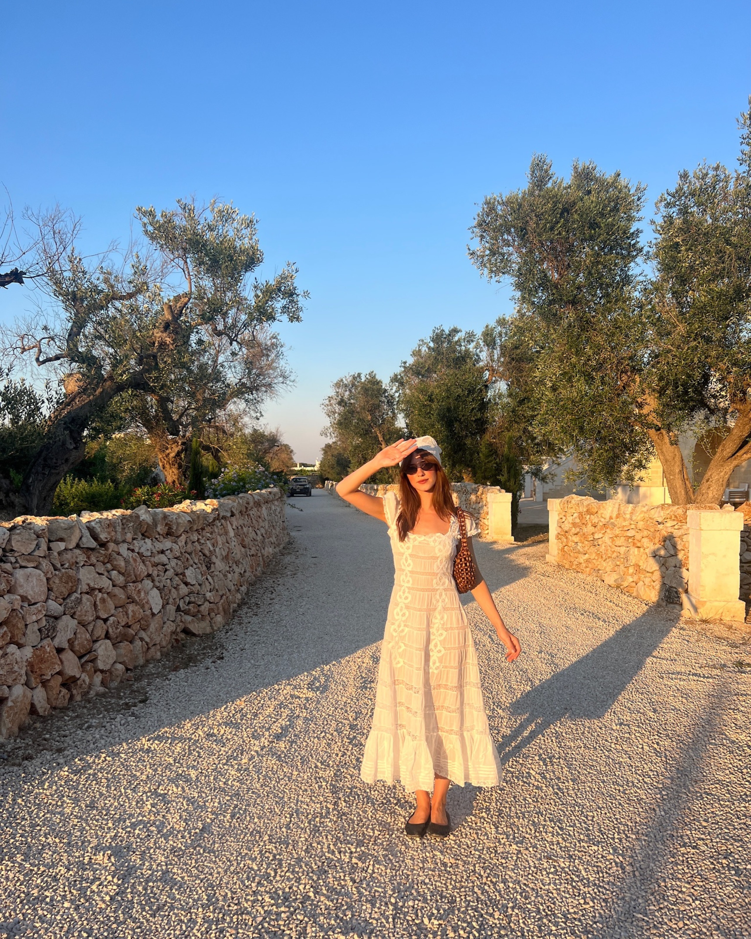 Daisy Edgar Jones wears a white midi dress with black flats, a white headscarf and a raffia bag.