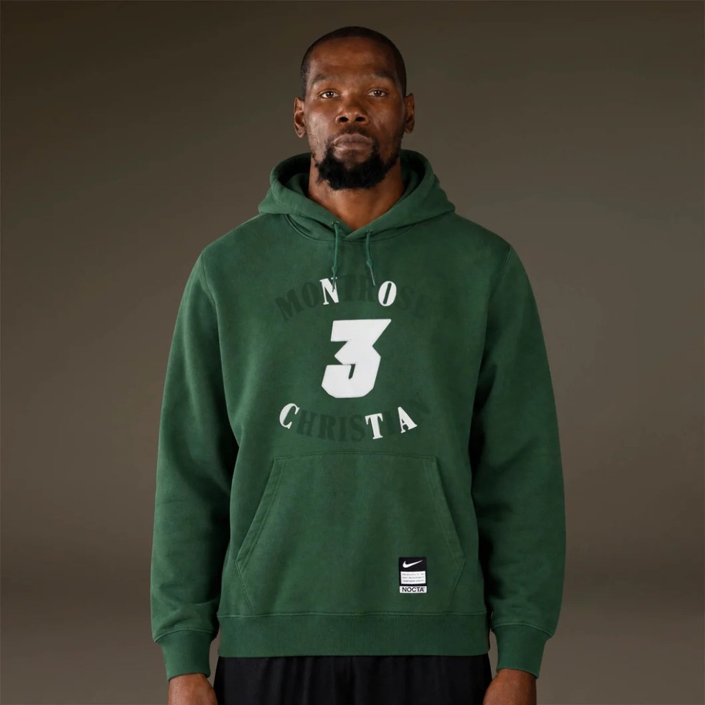 A man wearing a green hoodie with the text "NOCTA" and the number "3" on the front.