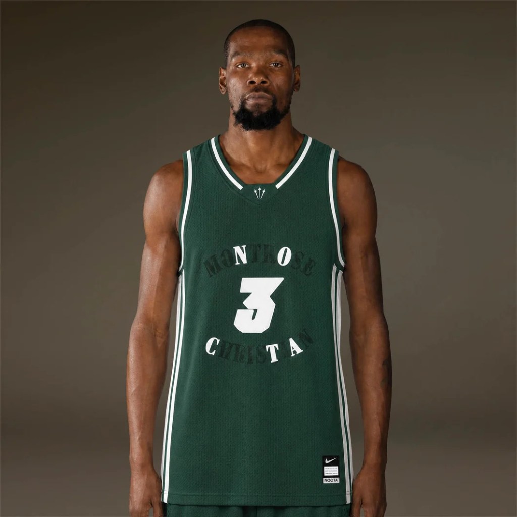 A man wearing a green basketball jersey with the text "MENTOR 3 CHRISTA" standing against a dark background.