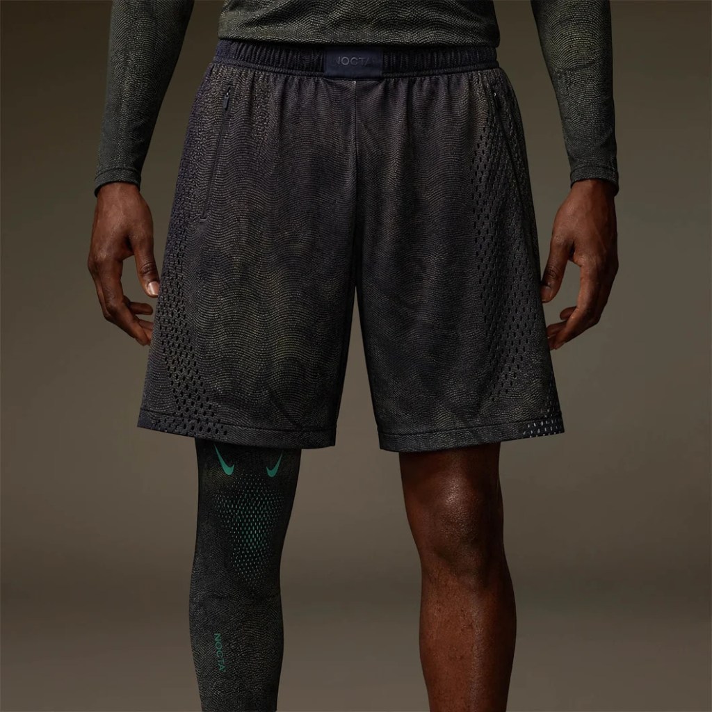 A person wearing black athletic shorts and compression socks, standing in a dark setting.