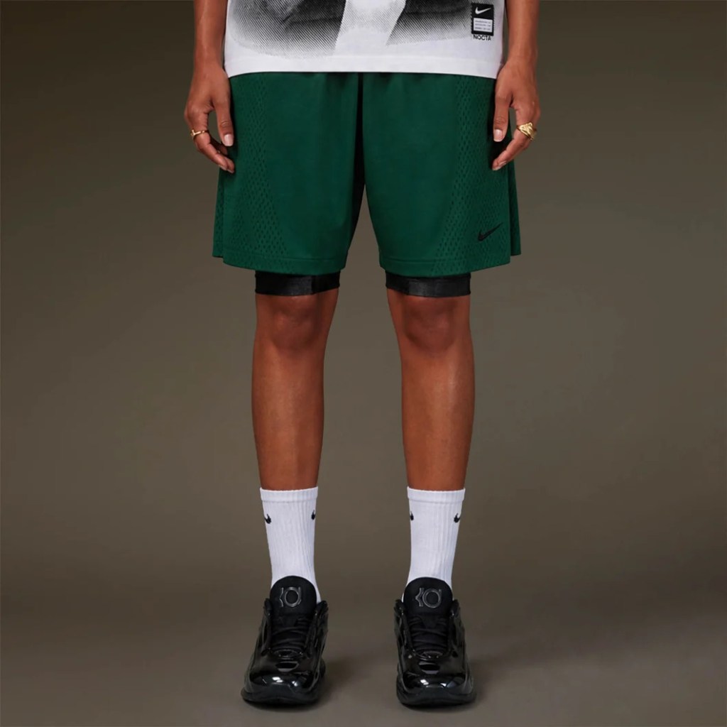 Green Nike basketball shorts with black and white accents, worn with white Nike socks and black Nike sneakers.