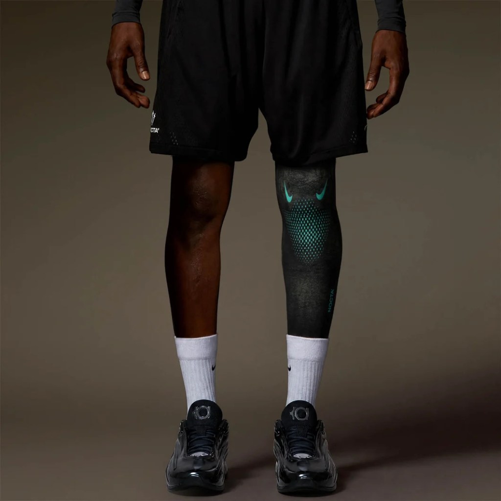 A person wearing black athletic clothing and Nike sneakers, with a patterned compression sleeve on their leg.