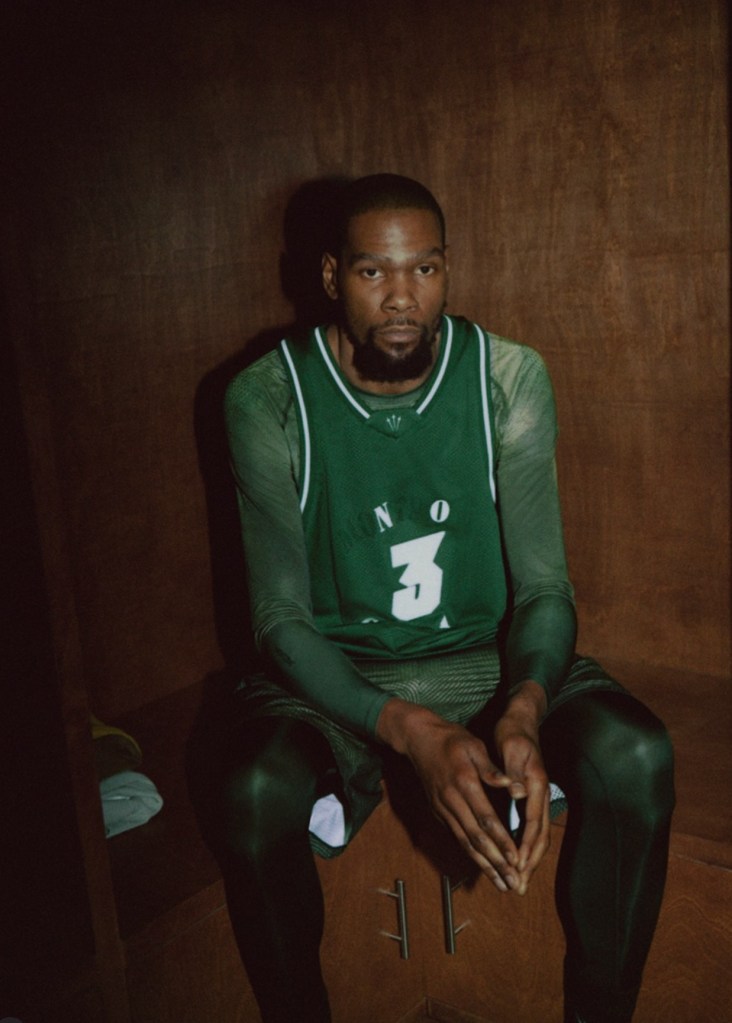 A man wearing a green jersey with the number 3 sits in a dimly lit room, looking directly at the camera.