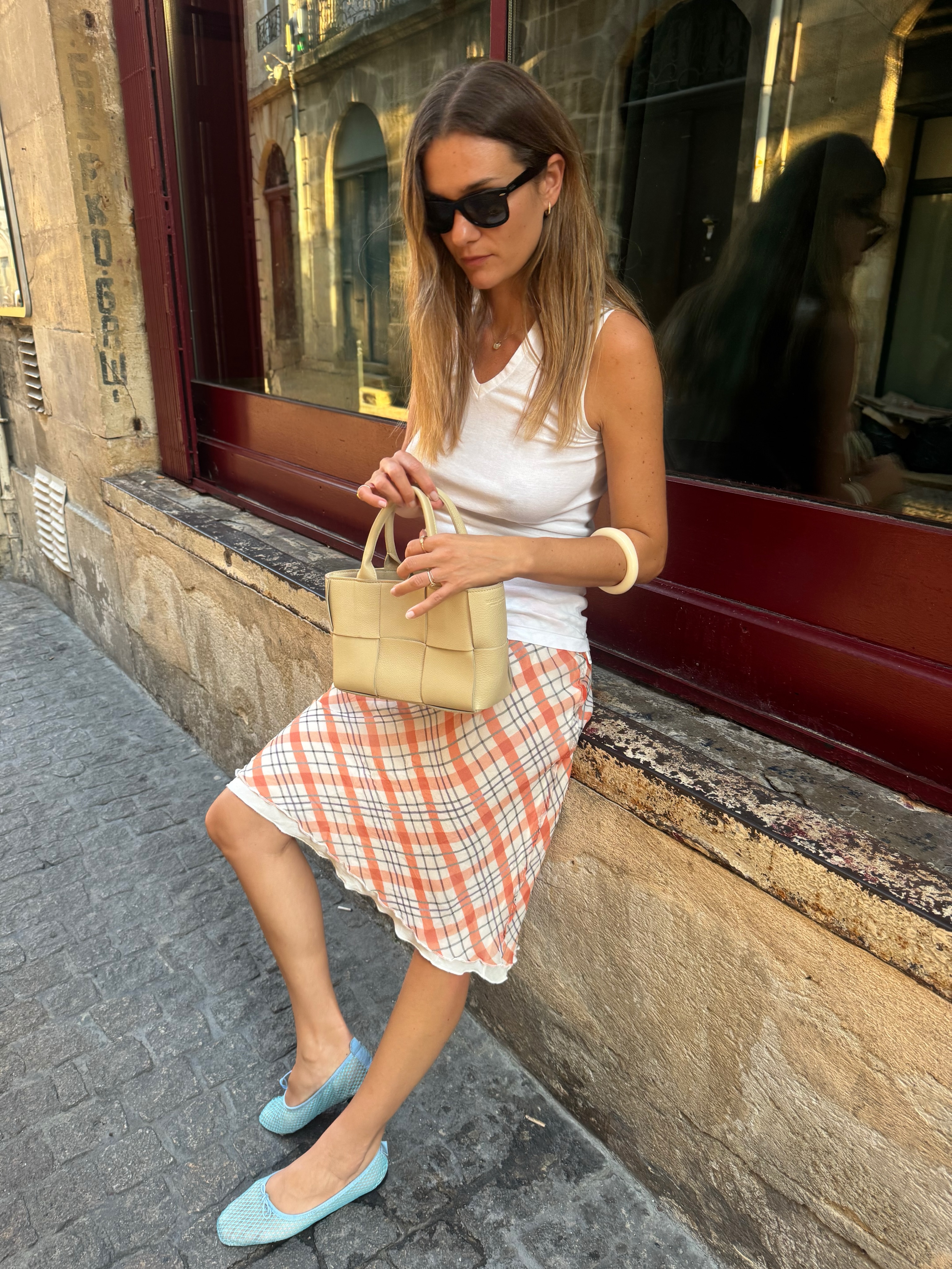 An image of @annelauremais wearing mesh flats with a white tank top with a checked midi skirt.