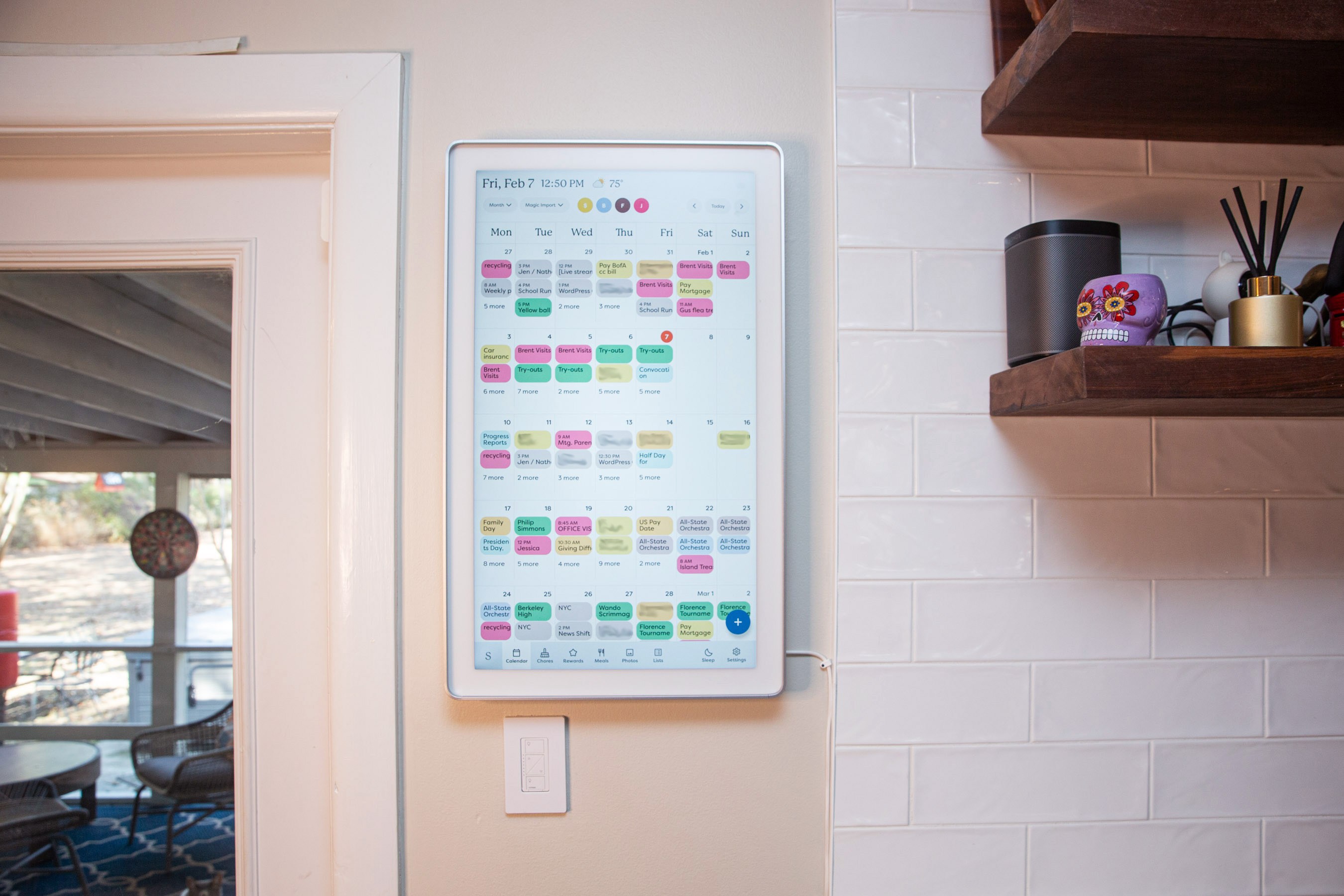 A large touchscreen calendar on a white tile wall.