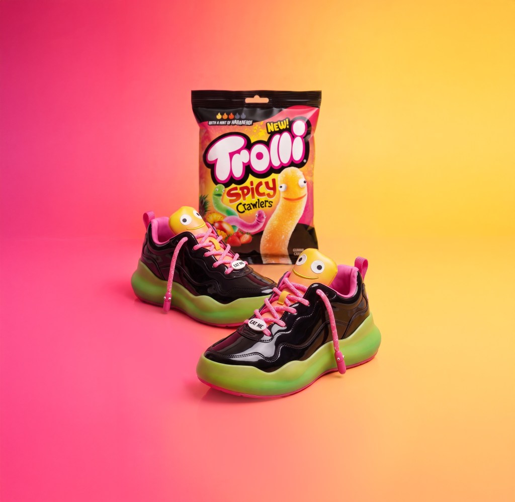 Pair of colorful sneakers with Trolli Spicy Crawlers snack bag on a vibrant pink and yellow background.